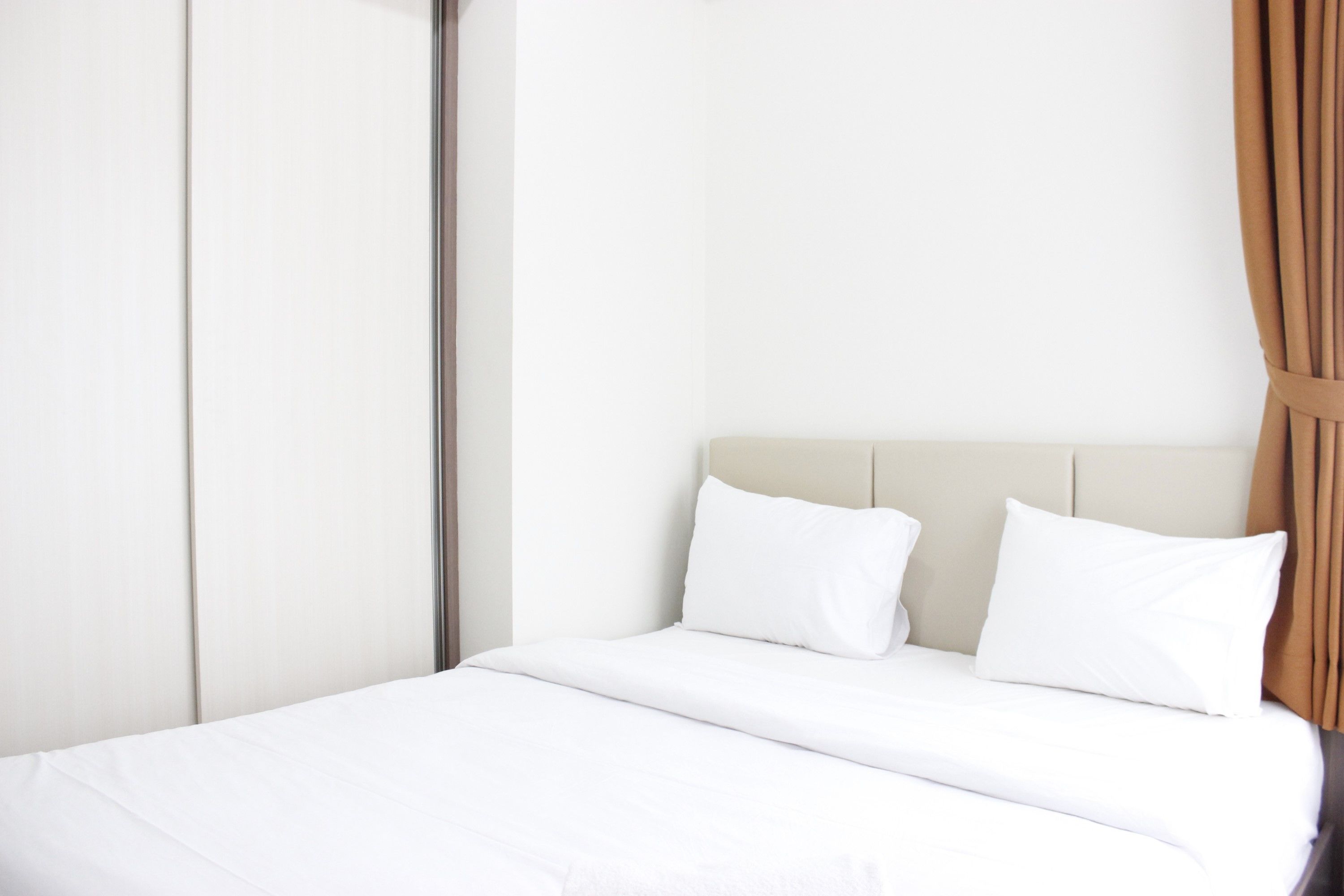 Un lit bien fait, avec du linge de lit blanc et une tête de lit beige, dans une chambre d’hôtel.