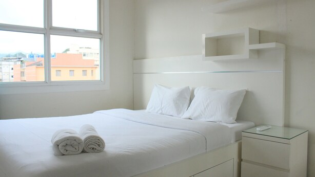 Une chambre d’hôtel avec un lit, deux oreillers, une table de chevet, une table en verre et une fenêtre donnant sur des immeubles.