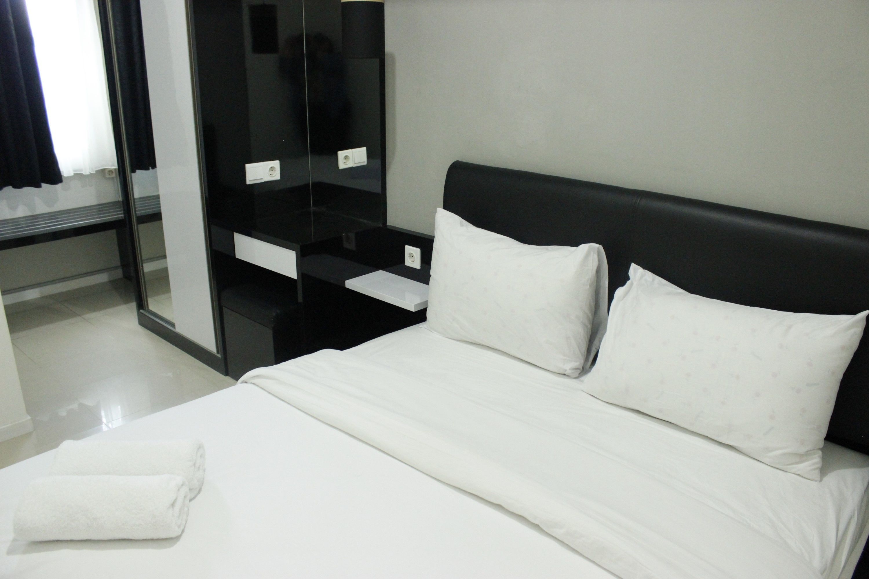 Une chambre d’hôtel avec un lit, du linge de lit blanc, une tête de lit noire, un miroir et une petite table.