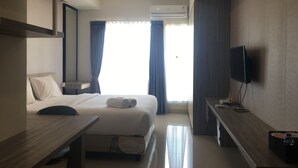 A hotel room with a bed, bedside table, TV, and an air conditioning unit. - Strategic Studio Galeri Ciumbuleuit 3 Apartment near Dago (Bandung)