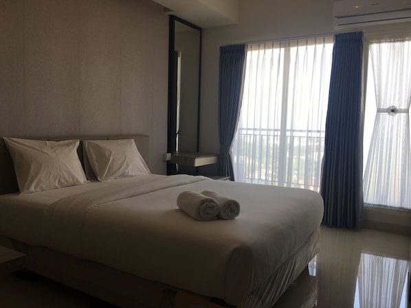 Una habitación de hotel con una cama grande, una mesita de noche, un espejo y una ventana con cortinas.