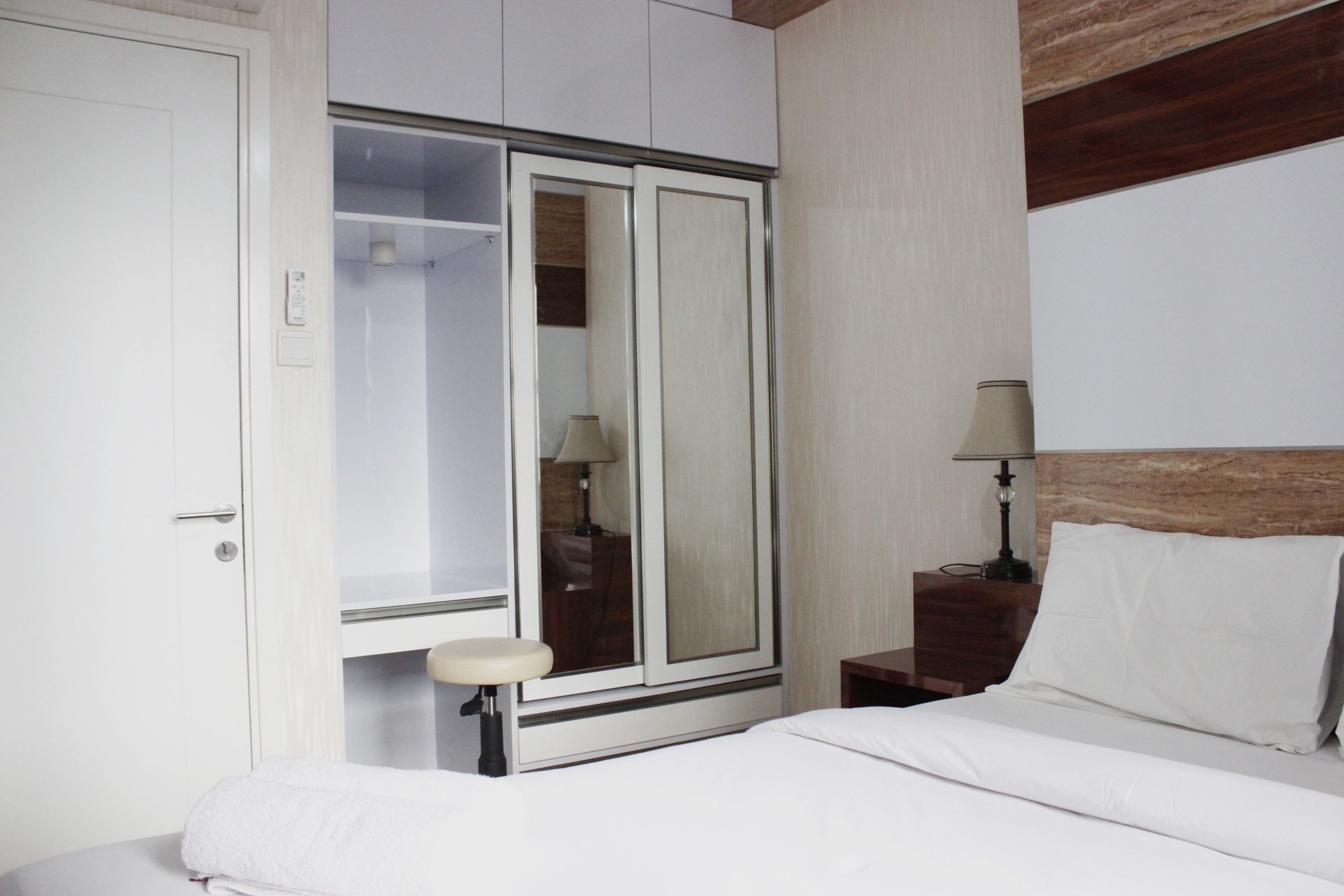 Una habitación de hotel con una cama, una mesita de noche con lámpara, un armario y un espejo.