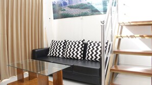 Un salón moderno con una mesa de centro de cristal, un sofá negro con cojines estampados y un ventanal con vistas a una cascada.