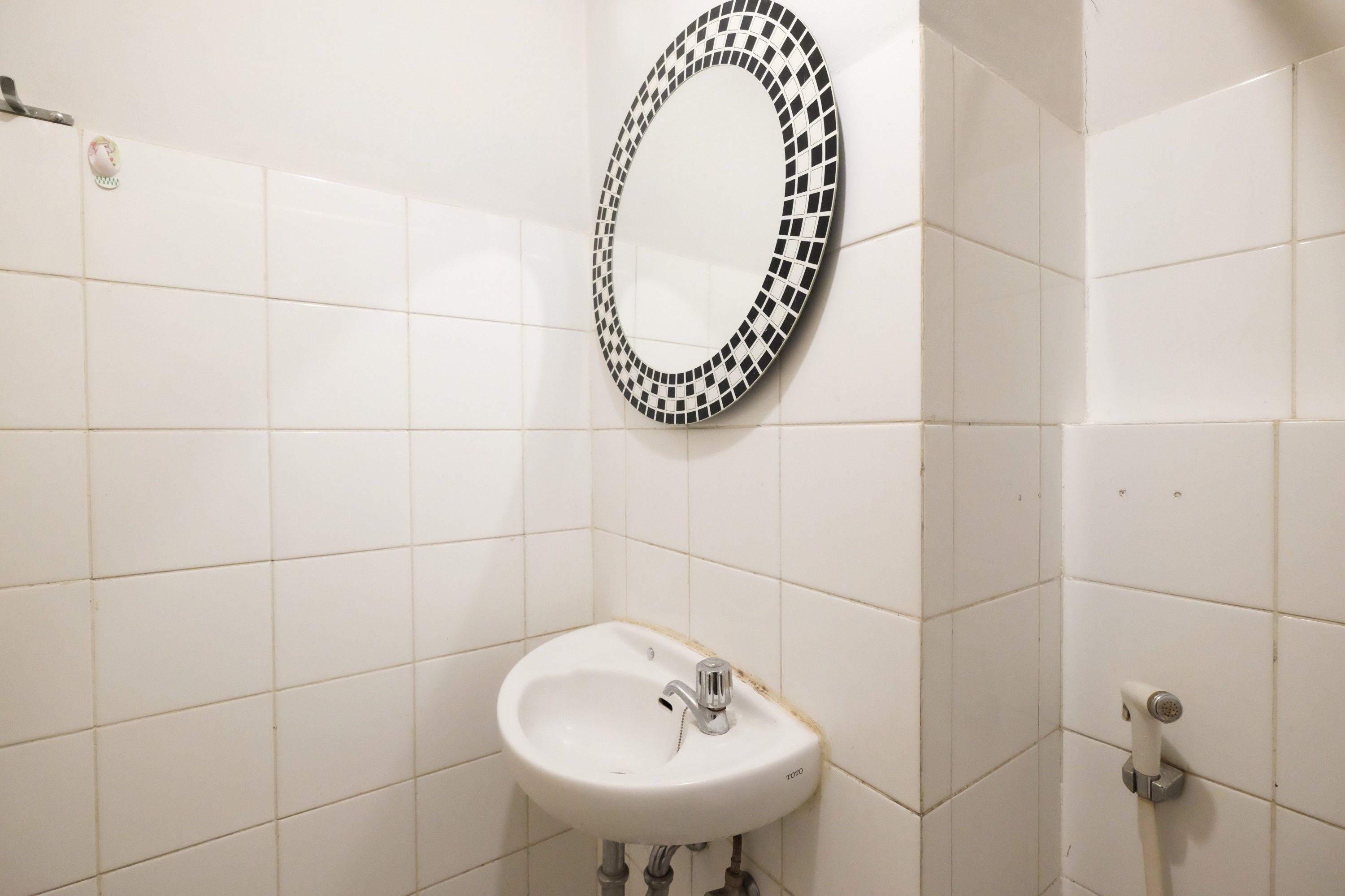 Une salle de bain avec des murs carrelés de carreaux blancs, un lavabo blanc avec un robinet et un miroir en mosaïque noir et blanc.