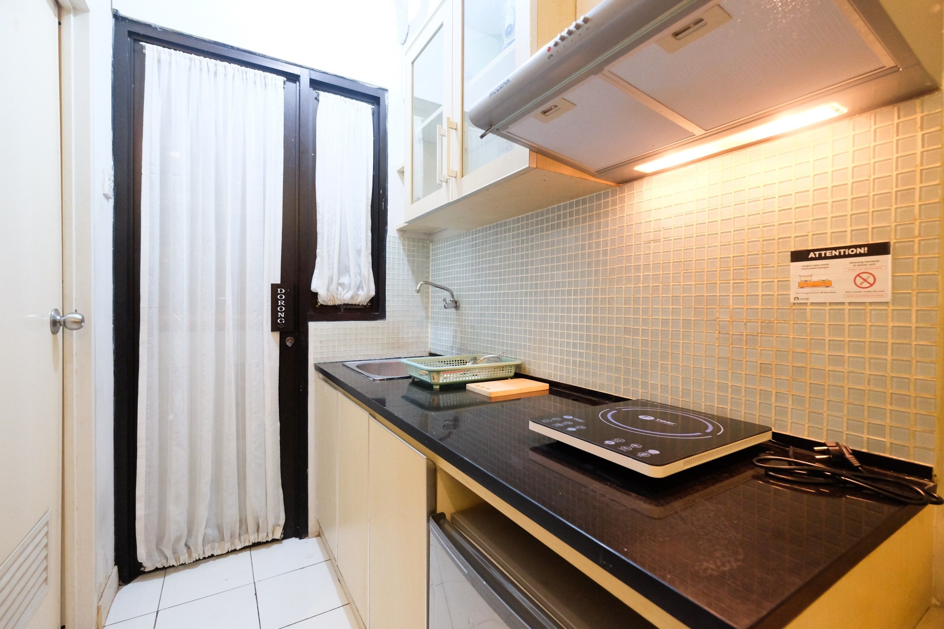 A compact kitchen with a black countertop, a built-in induction cooktop, a small sink, and a tiled backsplash.