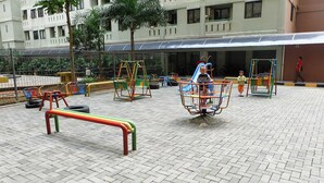 A playground with swings and a slide, surrounded by a fence and trees.