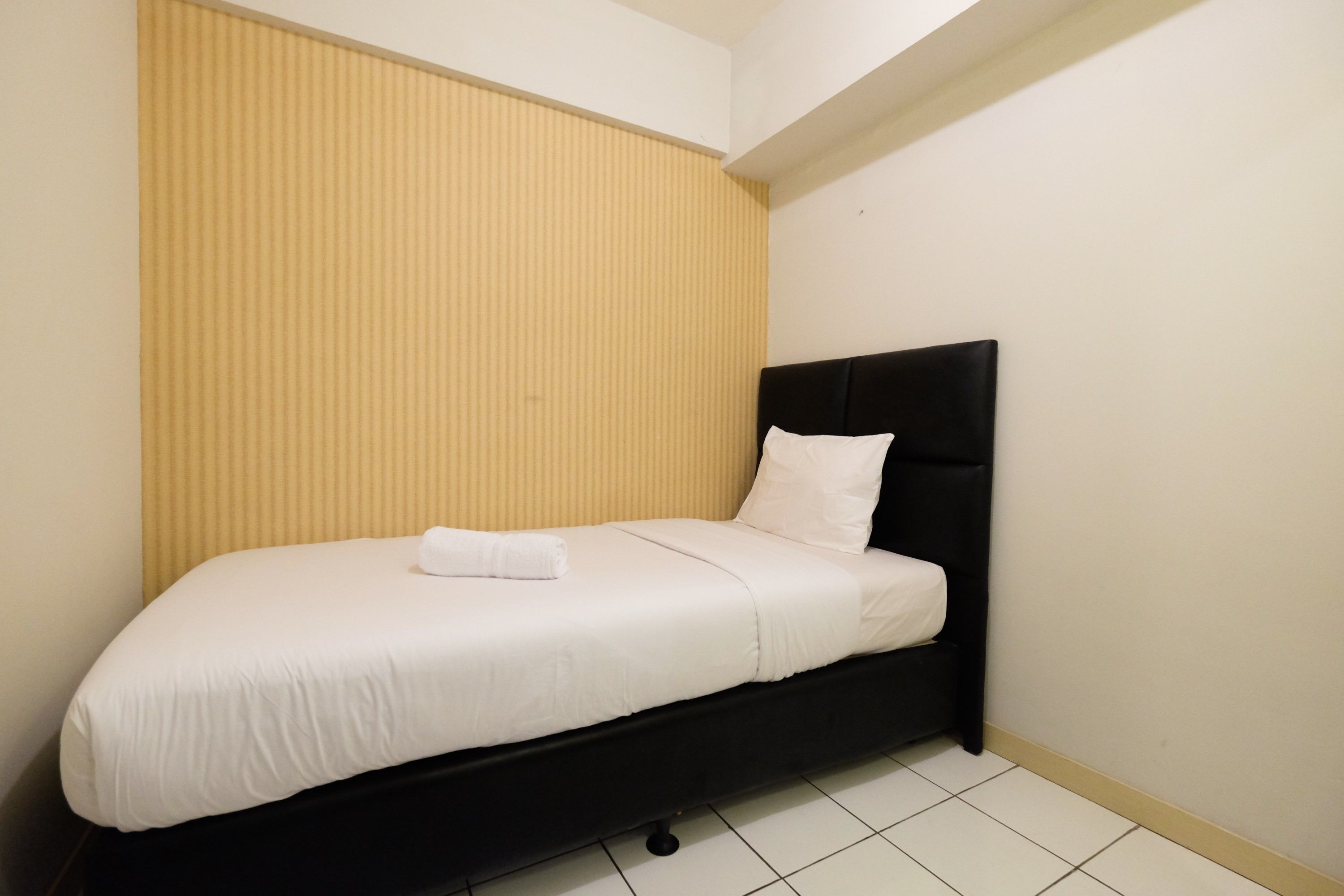 A single bed with a black headboard and white bedding in a room with a sloped ceiling and a beige wall.