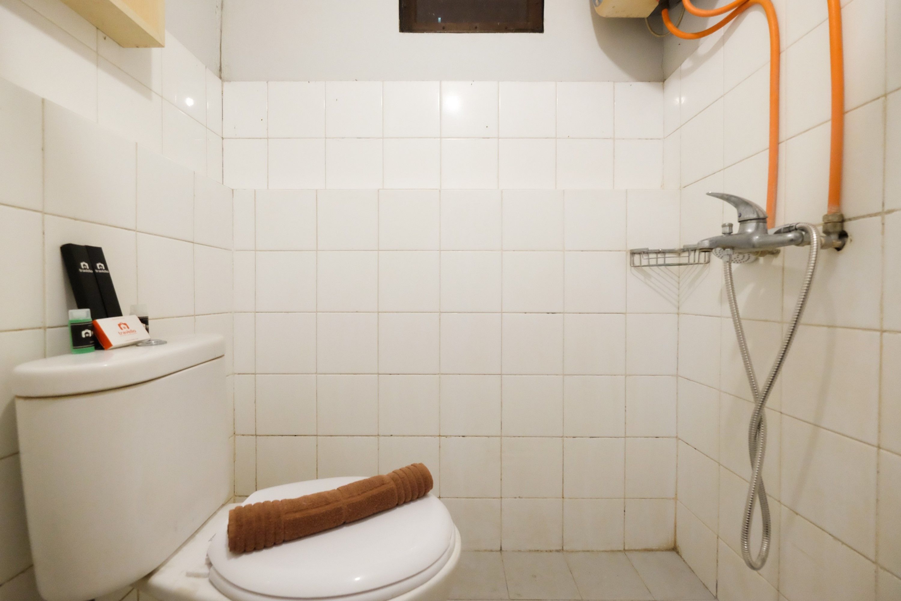 A small, clean bathroom with a white toilet, a shower with a handheld hose, and a towel on the toilet seat.