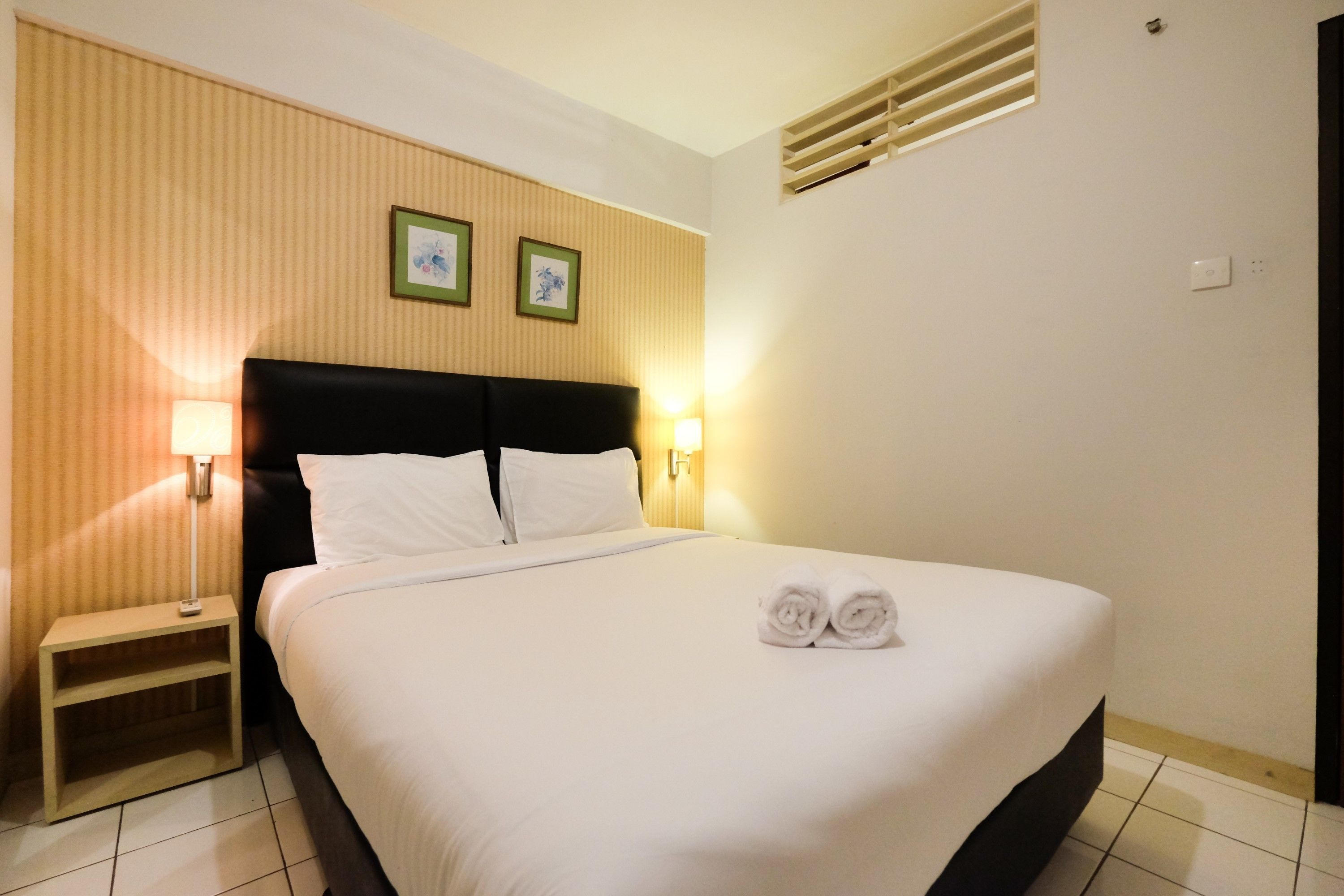 A neatly made bed with white linens, two bedside lamps, and a small nightstand.