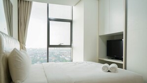 Un cuarto de hotel con una cama grande, un televisor en un estante y una ventana con vista a la ciudad.