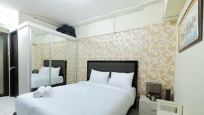 A neatly made bed with white linens and two rolled towels, a bedside table with a lamp, and a mirror on the wall. - Minimalist Studio at Kebagusan City Apartment (Jakarta)