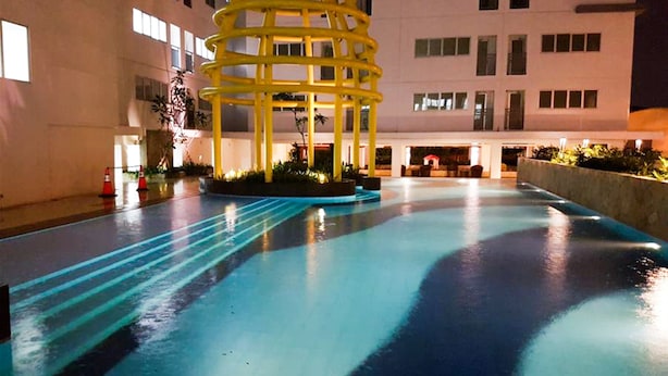 A pool area with a yellow structure, surrounded by a building with multiple windows. - Clean 2BR Bassura City Apartment (Jakarta)