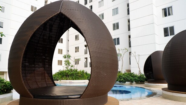 Ein moderner Außenbereich zum Sitzen mit einem runden Korbmöbel-Design, einem Pool und einem Gebäude im Hintergrund.
