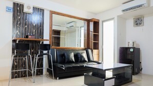 Ein modernes Wohnzimmer mit einer schwarzen Ledersofa, einem Glastisch und einem eingebauten Fernseher. Es gibt eine kleine Bar mit Hockern und einem Kühlschrank.