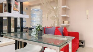 Una sala de estar moderna con una mesa de comedor de vidrio, sillas blancas, un sofá rojo con cojines y estantes decorativos.