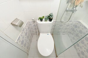 A small bathroom with a toilet, a toilet paper holder, and a shower area. - Homey 1BR Apartment @ Bassura City (Jakarta)