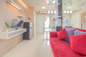 A modern living room with a red sofa, a flat-screen TV, a small table, and a water dispenser. - Homey 1BR Apartment @ Bassura City (Jakarta)