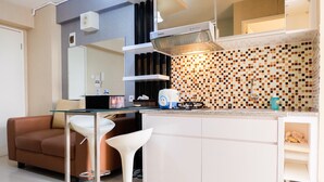 A modern kitchen with a glass-top table, a white sink, and a brown sofa. - Contemporary 2BR at Bassura City Apartment (Jakarta)