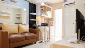 A modern living room with a brown leather sofa, a flat-screen TV, and a dining area with a table and chairs. - Contemporary 2BR at Bassura City Apartment (Jakarta)