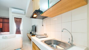 A compact hotel room with a bed, a small kitchenette, a sink, and a TV. - Elegant Studio Room The Springlake Summarecon Apartment (Bekasi)