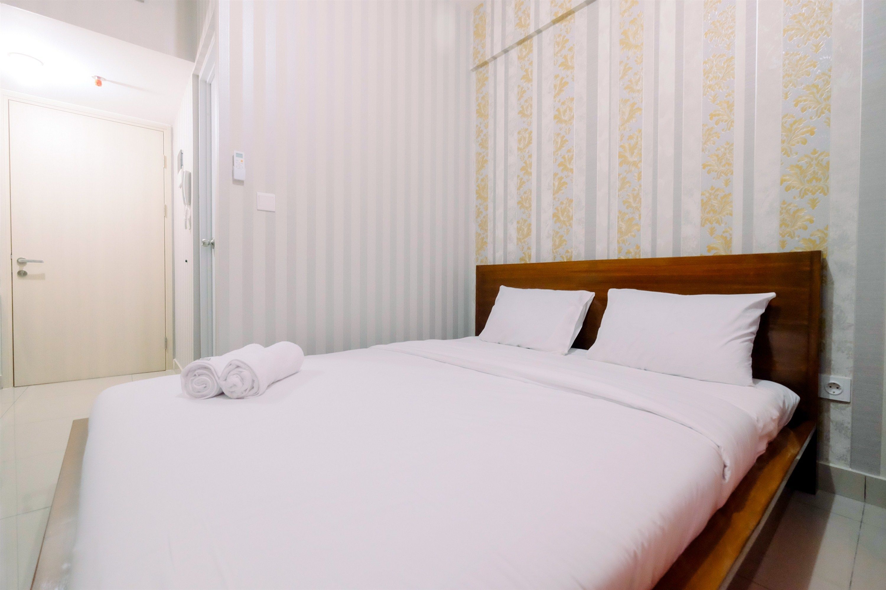 A neatly made bed with white linens and pillows, a wooden headboard, and a striped curtain with a floral pattern.