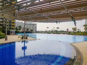 A swimming pool with a covered area, surrounded by greenery and a building labeled "BSPK PENABUR". - Cozy Studio Springlake Summarecon Bekasi Apartment (Bekasi)