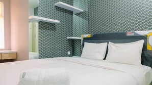 Een net opgemaakt bed met witte lakens en kussens, een opgevouwen handdoek op het bed, en een muur met een geometrisch patroon.