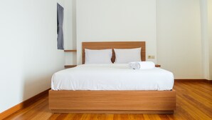 Ein ordentlich bezogenes Bett mit weißen Leinentüchern und einem hölzernen Kopfteil in einem sauberen, minimalistischen Zimmer mit Holzböden.
