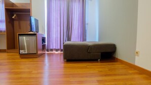 Ein Zimmer mit Holzboden, einem grauen Sofa, einem Fernseher auf einem Schrank und einem kleinen Kühlschrank.