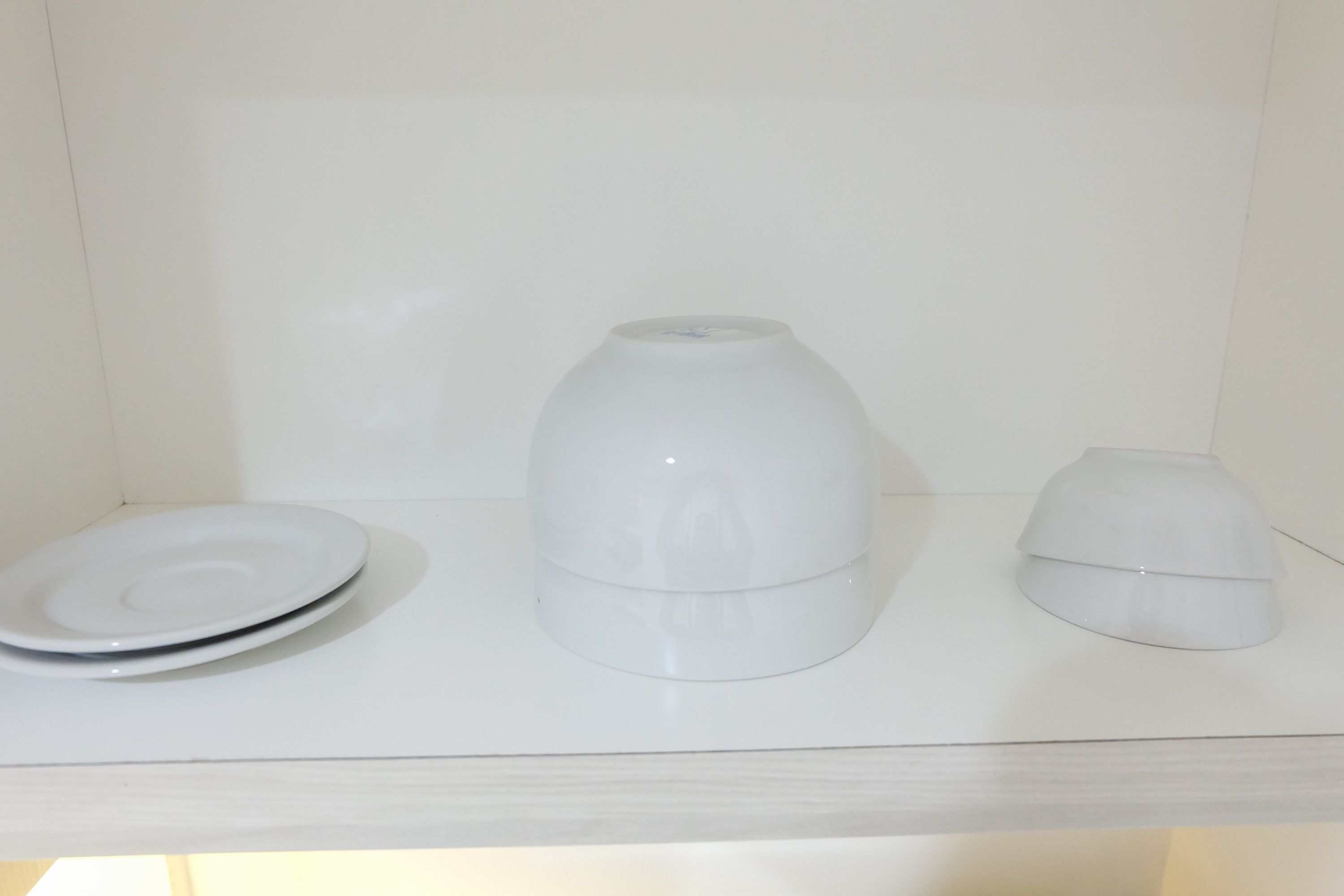 A white shelf with a white plate, a white vase, and a white candle holder.