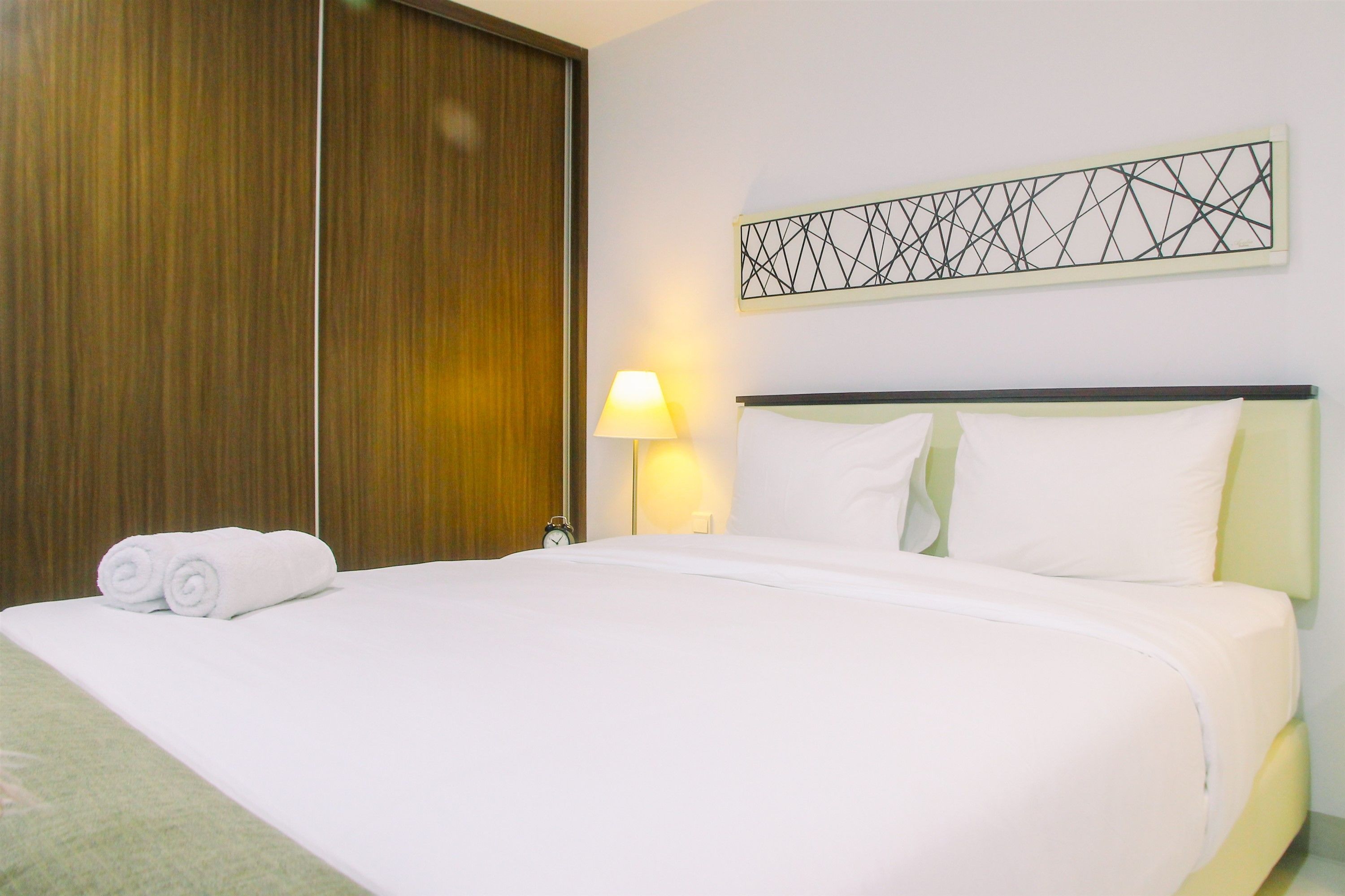 A neatly made bed with white linens, a wooden wardrobe, and a wall-mounted geometric artwork.