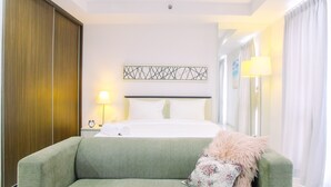 Una camera d'albergo con un letto, un divano verde, un'opera d'arte a parete e una lampada.