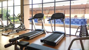 Una palestra con tapis roulant, cyclette e macchinari per pesi. Ampie finestre offrono vista su una zona piscina esterna.