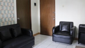 A room with a black leather sofa, a leather armchair, a wooden door, and a radiator. - Minimalist 2BR Apartment at Gateway Ahmad Yani (Bandung)