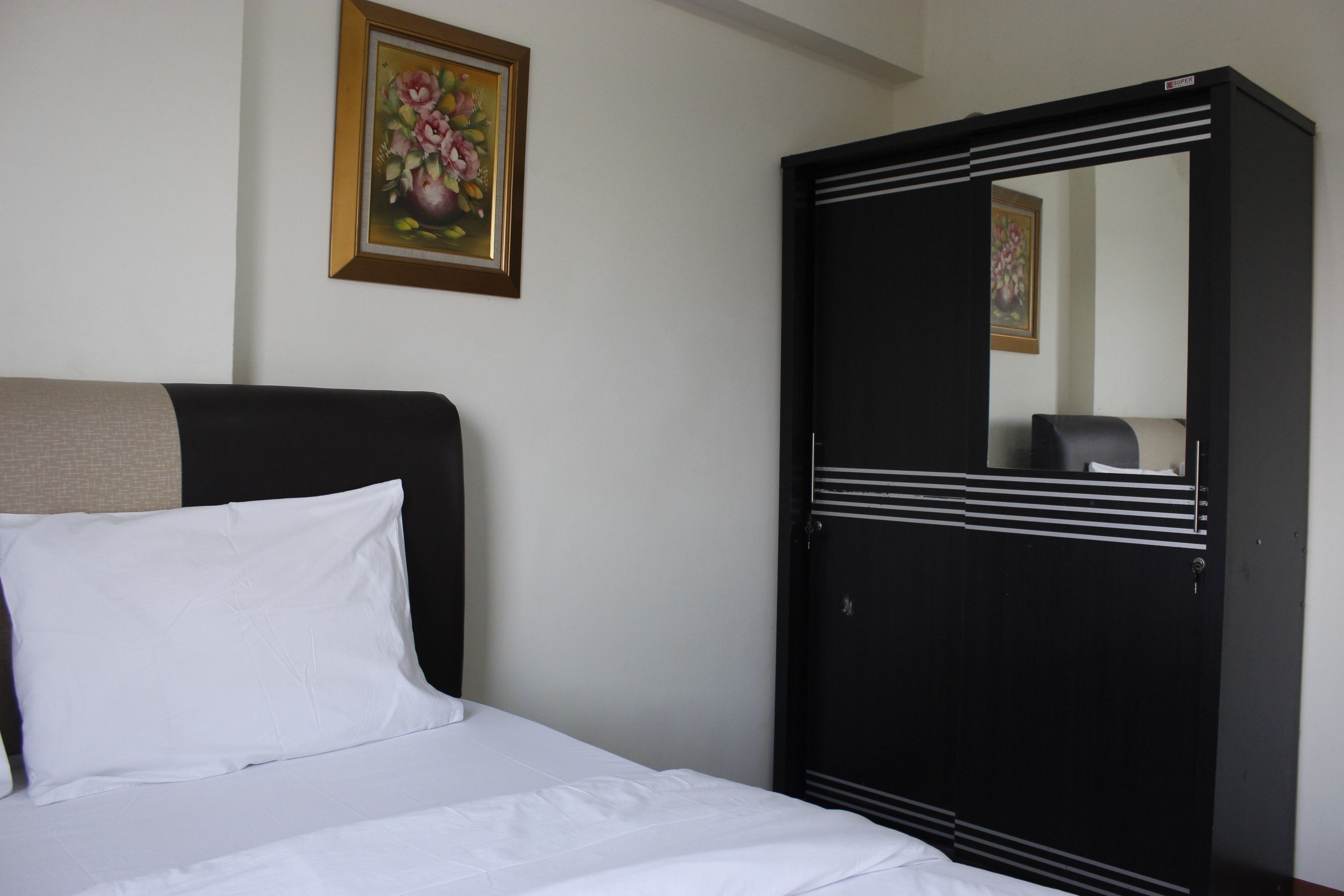Een slaapkamer met een bed, een kledingkast en een lijst met bloemen op de muur.