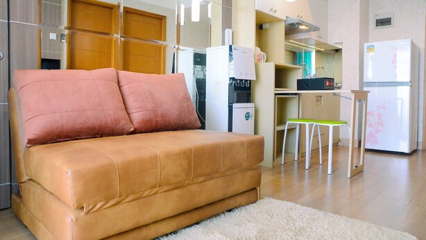 Un salon moderne comprenant un canapé, une table basse et un coin cuisine équipé d’un réfrigérateur, d’un four à micro-ondes et d’un distributeur d’eau.