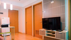 Une chambre d’hôtel moderne dotée d’une télévision à écran plat, d’une armoire en bois et d’une petite kitchenette équipée d’un réfrigérateur et d’un four à micro-ondes.