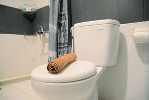 A bathroom with a white toilet, a towel on the lid, a shower curtain, and a soap dish on the wall. - Full Parquette 2BR @ Cinere Bellevue Apartment (Depok)