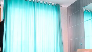 Une chambre moderne avec un canapé-lit, un téléviseur posé sur un meuble et une grande fenêtre avec des rideaux.