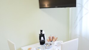 A dining area with a white table, two white chairs, a black coffee maker, a bowl of pastries, and a flat-screen TV mounted on the wall. - Casa Aurora B&B (Chieti)