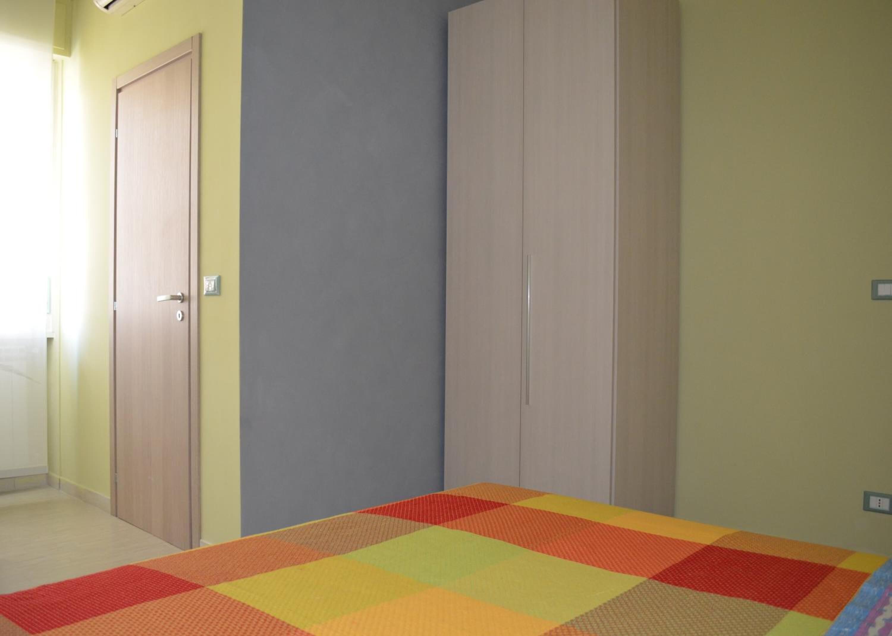 A room with a bed, two doors, and a wall with a light switch.