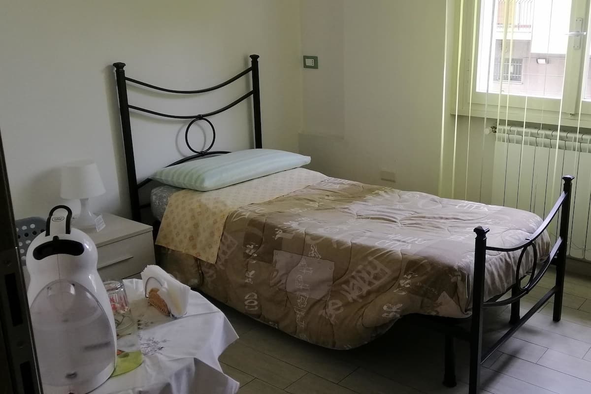 A small, neatly arranged bedroom with a single bed, a bedside table, a lamp, and a radiator.