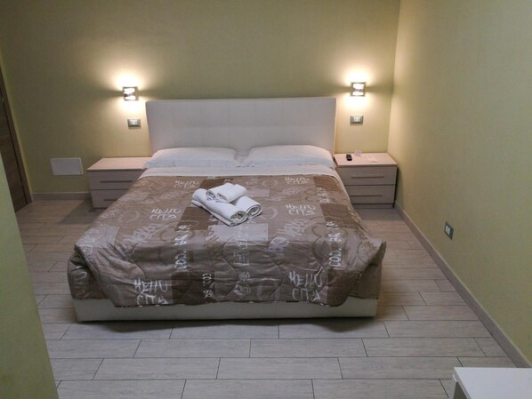 Una cama bien hecha con una colcha estampada, dos mesitas de noche con lámparas y una pequeña cómoda.
