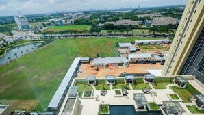 A high-rise hotel with a rooftop pool, a sports field, and a view of the city skyline. - Elegant 1BR Branz BSD Apartment near AEON Mall (Pagedangan)