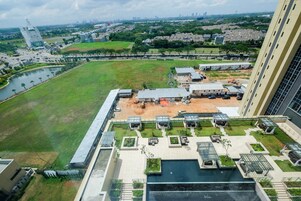 A high-rise hotel with a rooftop pool, a sports field, and a view of the city skyline.