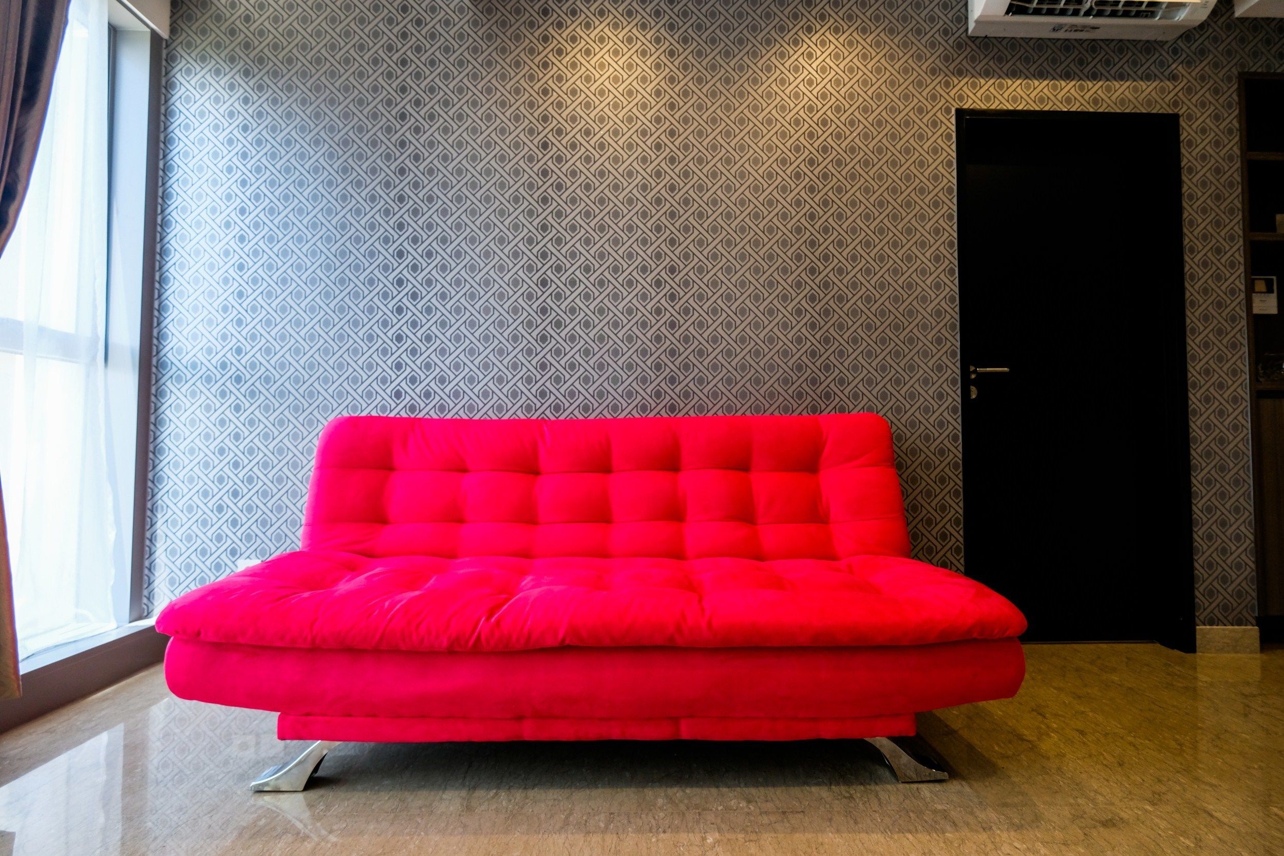 A bright red sofa in a modern room with patterned wallpaper and a door in the background.