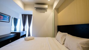A hotel room with a bed, a desk, an air conditioner, and a window with curtains. - Elegant 1BR Branz BSD Apartment near AEON Mall (Pagedangan)