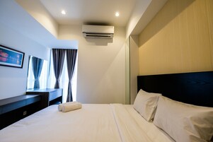 A hotel room with a bed, a desk, an air conditioner, and a window with curtains.