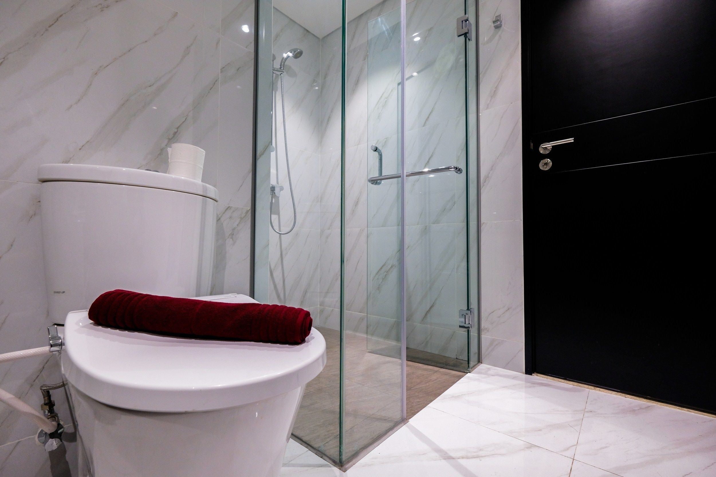 A modern bathroom with a glass-enclosed shower, a white toilet, and a red towel on the seat.