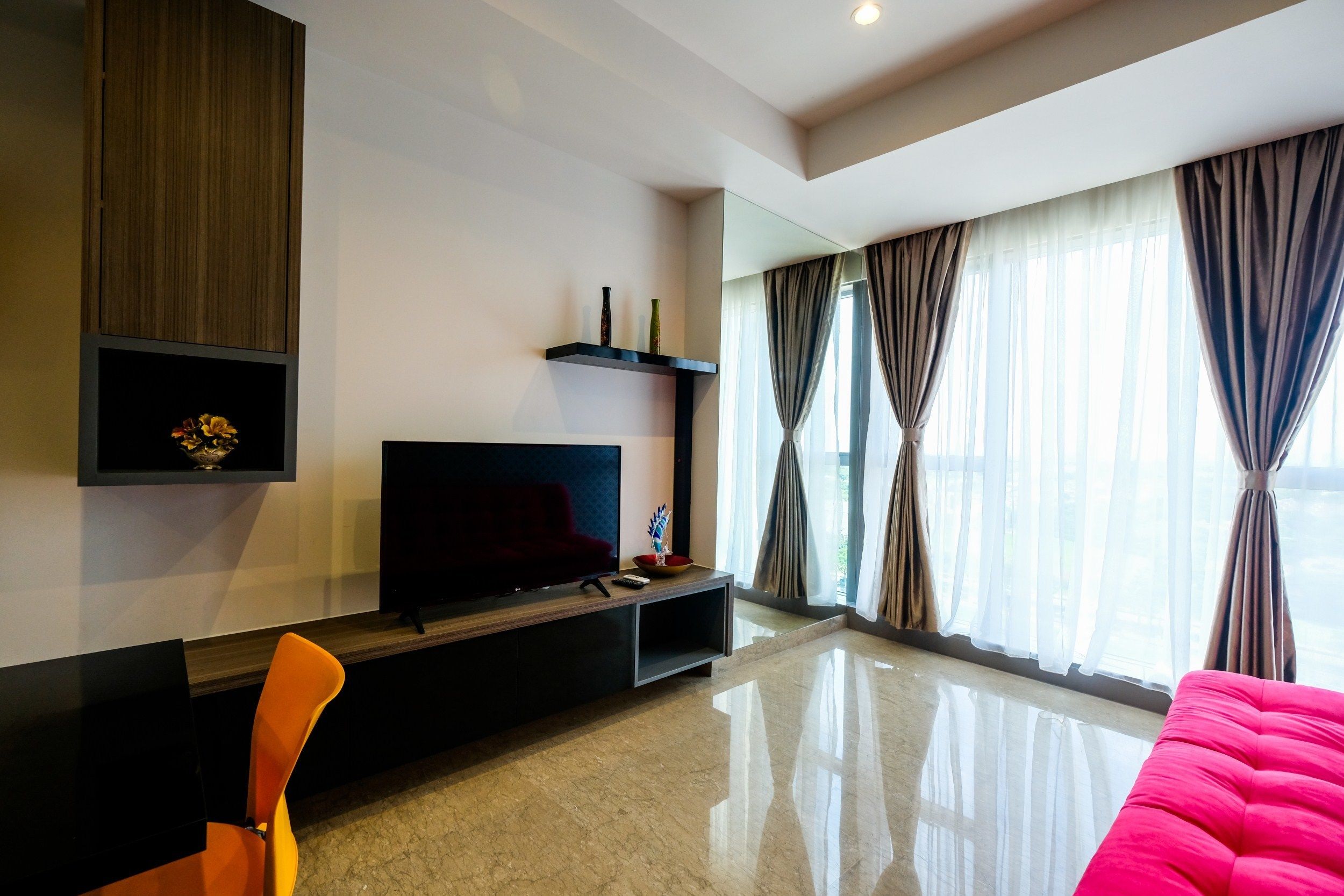 A modern living room with a flat-screen TV, a wooden cabinet, a red sofa, and a large window with curtains.